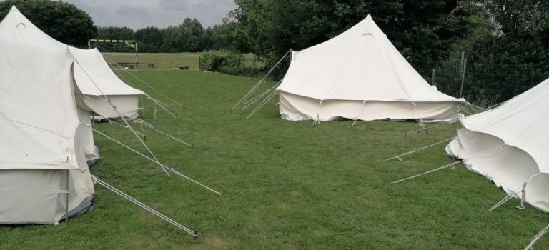 Padfinder-Jurten auf einer grünen Wiese, bedeckter Himmel, Bäue im Hindergrund